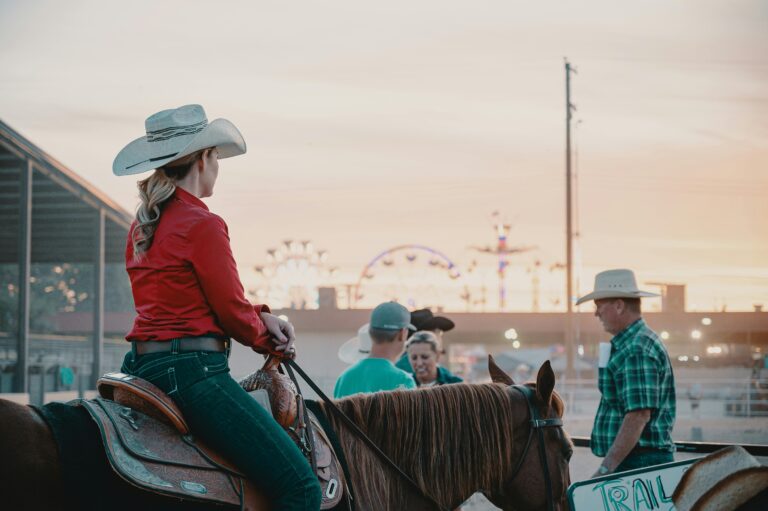 A female cowboy on horseback participates in a lively rodeo at sunset.