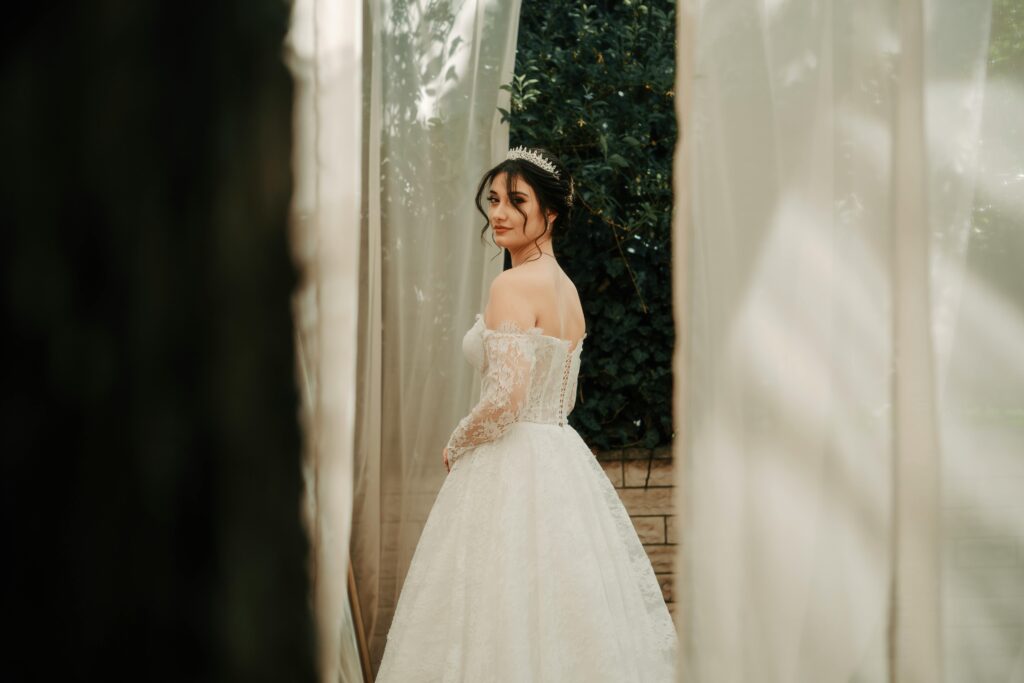 A beautiful bride in a lace gown and tiara stands outdoors, creating a dreamy wedding scene.